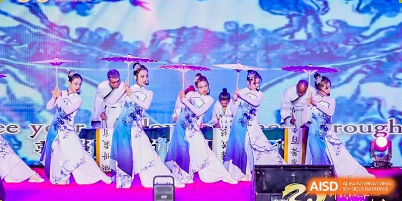 Performers in traditional blue and white outfits hold decorative umbrellas during a cultural dance on stage Maple Leaf International Schools - Hainan