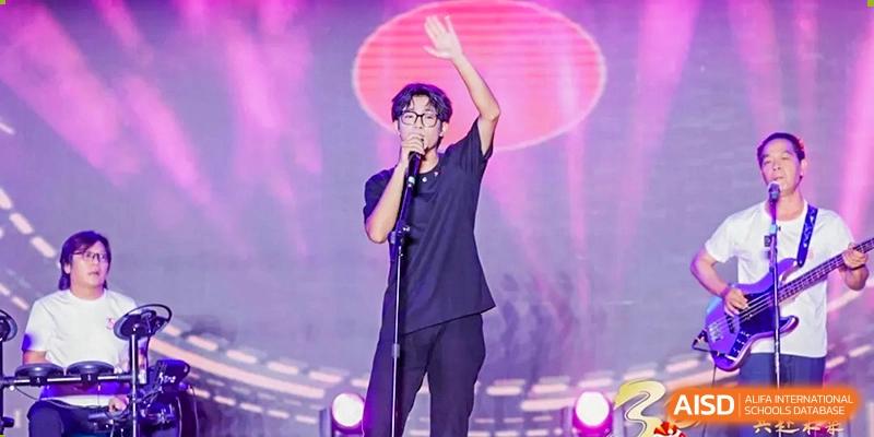 A male student stands alone on stage under a spotlight with a microphone waving to the audience Maple Leaf International Schools - Hainan