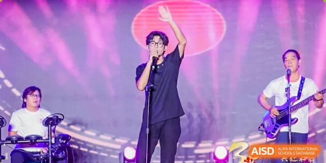 A male student stands alone on stage under a spotlight with a microphone waving to the audience Maple Leaf International Schools - Hainan