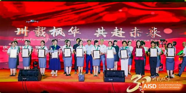 Staff members stand in a line on stage holding certificates during a formal school awards ceremony Maple Leaf International Schools - Hainan
