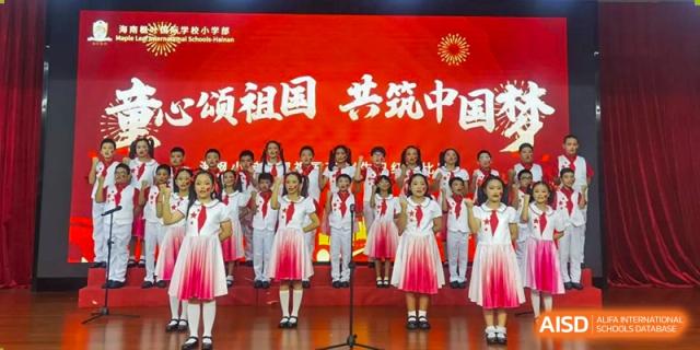 A large group of students in red and white uniforms perform a choral song in front of a red banner Maple Leaf International Schools - Hainan