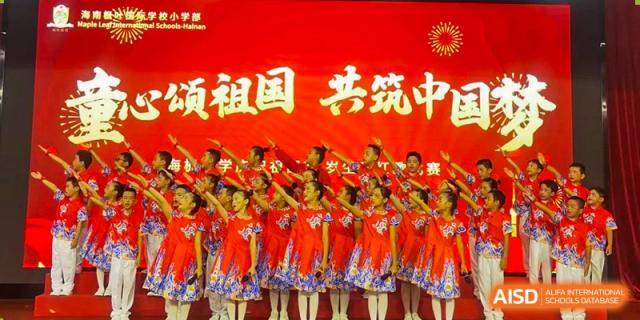 A large group of students in red floral dresses performing a coordinated dance on stage with a red backdrop at Maple Leaf International Schools - Hainan