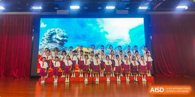 Students in formal uniforms stand in rows on a stage performing a choral piece during a school celebration Maple Leaf International Schools - Hainan