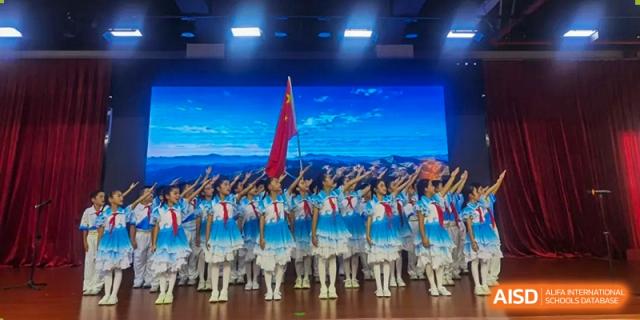 Students in blue and white outfits marching on stage with one student holding a large red flag at Maple Leaf International Schools - Hainan