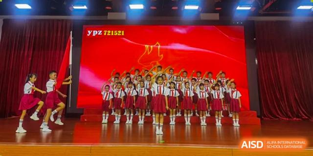 Students in white shirts and red skirts or shorts standing in formation on a stage during a school performance at Maple Leaf International Schools - Hainan