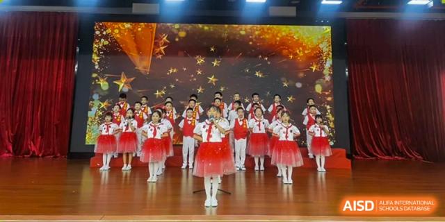 A young soloist in a white and red tutu sings into a microphone backed by a choir of students at Maple Leaf International Schools - Hainan
