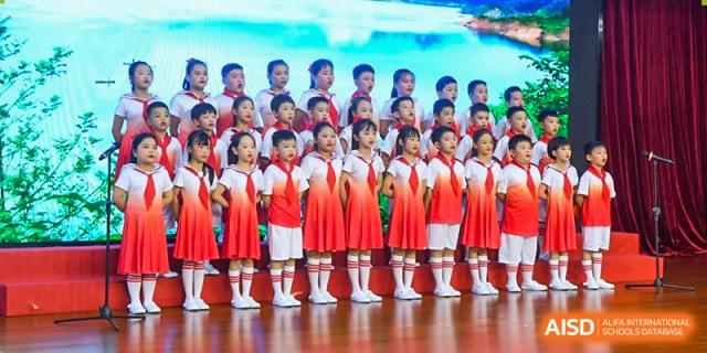 A row of young students in red and white uniforms singing together on stage during a performance at Maple Leaf International Schools - Hainan
