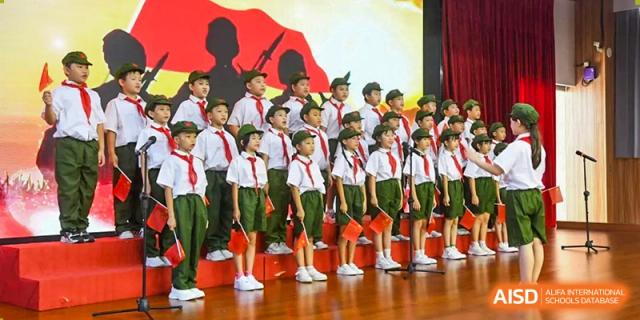 Students dressed in green and white scout-style uniforms standing at attention on stage for a ceremony at Maple Leaf International Schools - Hainan