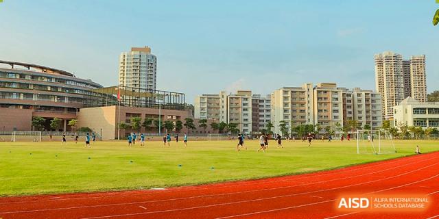 Students participating in track and field activities on a professional red running track bordering a large grass field at Guangzhou ULink International School.