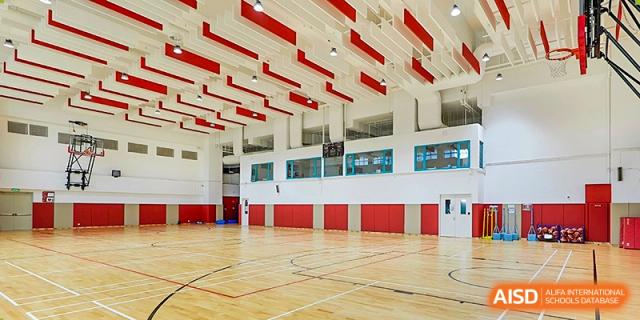 A spacious indoor basketball court featuring polished wood floors and a modern red and white acoustic ceiling design at Guangzhou ULink International School.