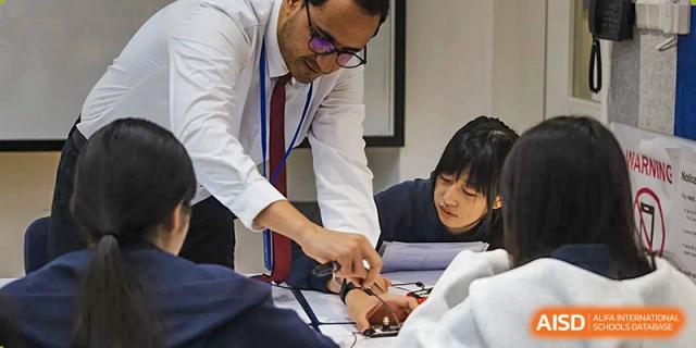 A male teacher leaning over a desk to provide one-on-one guidance to a student during a classroom activity at Guangzhou ULink International School.