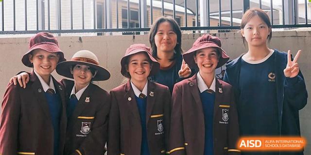Three students in formal school blazers and hats smiling together during a school event or field trip at Guangzhou ULink International School.