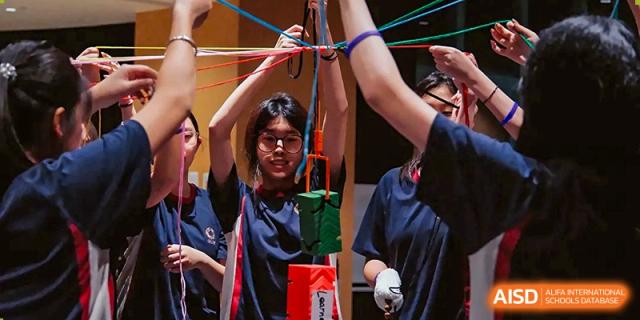 A student focuses on a team-building exercise involving lifting blocks with a collaborative rope system at Guangzhou ULink International School.