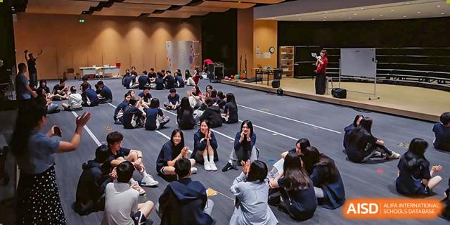 Students sitting in circles on a stage floor during an interactive workshop or group discussion session at Guangzhou ULink International School.