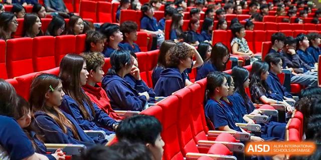 A large group of students sitting in red tiered theater seating during a presentation or school assembly at Guangzhou ULink International School.