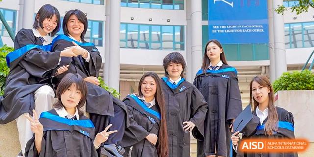 Group of happy graduates in black academic gowns and blue stoles posing outside the campus buildings at Guangzhou ULink International School.