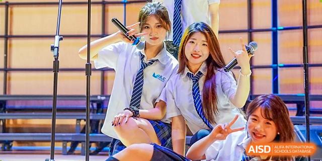 Two students in formal school uniforms with striped ties smiling during a performance or school celebration at Guangzhou ULink International School.