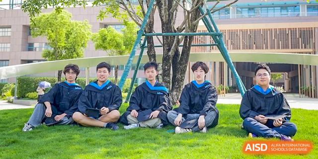 Three male graduates in black and blue academic gowns sit on the grass during a graduation ceremony at Guangzhou ULink International School.