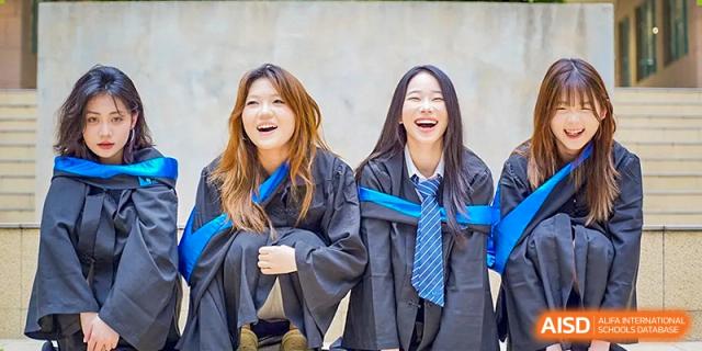 Two female graduates sharing a joyful moment and laughing while wearing their graduation gowns at Guangzhou ULink International School.