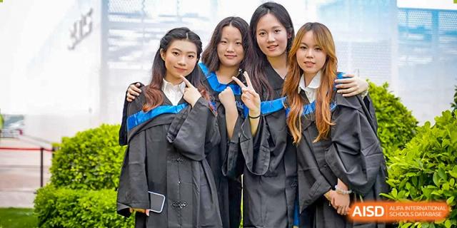 Four female graduates in academic gowns smiling and posing together during their commencement ceremony at Guangzhou ULink International School.