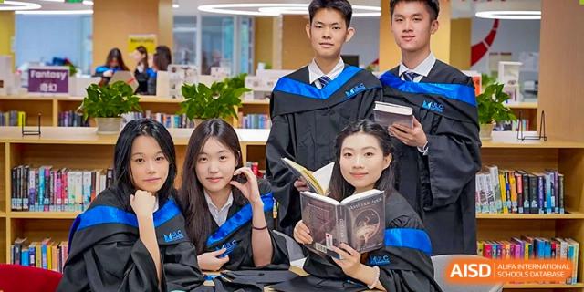 A group of graduates in academic regalia posing with books in a library setting to celebrate their achievement at Guangzhou ULink International School.