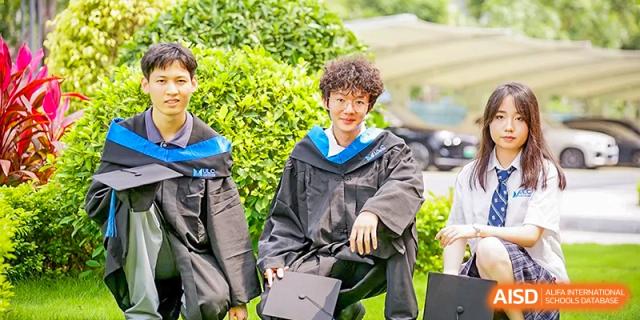 A male graduate in a black gown smiling warmly while sitting outdoors during a sunny graduation day at Guangzhou ULink International School.