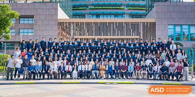 A large, formal group photo of the graduating class and faculty members gathered in front of a campus building at Guangzhou ULink International School.