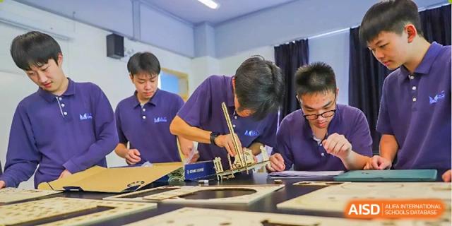 Students working together on a technical STEM project, carefully assembling a wooden model in a workshop at Guangzhou ULink International School.
