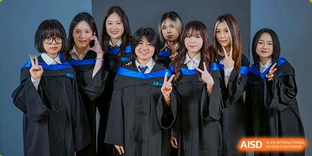 A group of graduates in academic gowns making peace signs and smiling for a celebratory photo at Guangzhou ULink International School.
