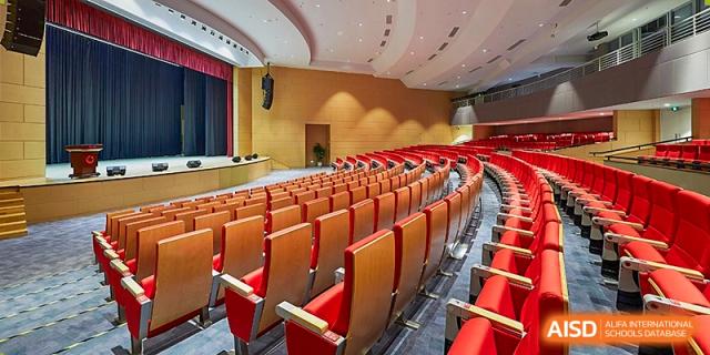 A wide interior view of the modern campus auditorium with rows of red velvet seats and professional stage lighting at Guangzhou ULink International School.