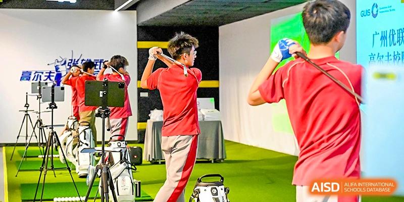 A student in a red uniform practices his golf swing follow-through in an indoor training facility, focusing on form and technique at Guangzhou ULink International School.