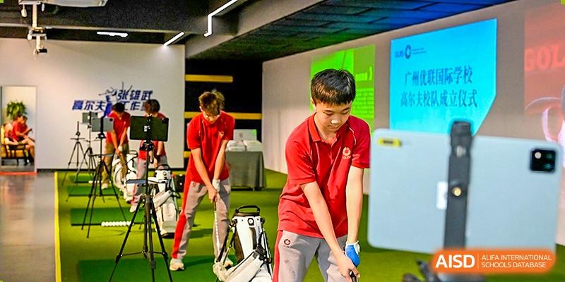 Two students practicing their golf putting and stance on an indoor green, with equipment bags nearby in a modern sports facility at Guangzhou ULink International School.