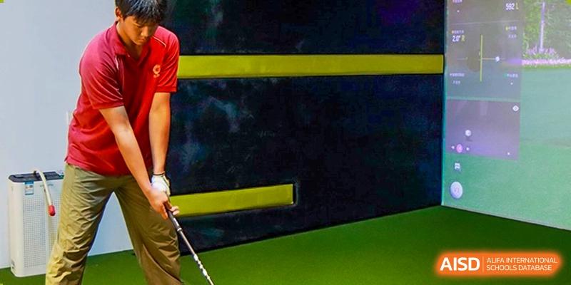 A close-up view of the indoor golf facility featuring a green turf and dark padded walls with yellow safety stripes for student practice at Guangzhou ULink International School.