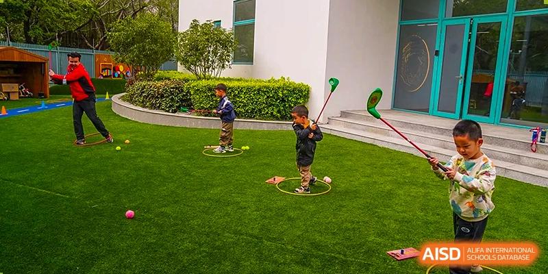 Young students practicing their golf swing with colorful clubs inside training hoops on an outdoor green space at Guangzhou ULink International School.