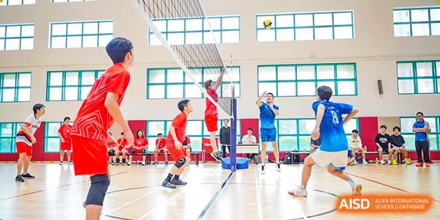 Students in red and blue uniforms competing in an indoor volleyball match, showing a player jumping at the net at Guangzhou ULink International School.