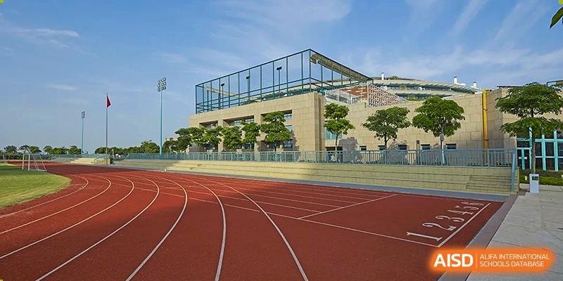 A wide view of the professional red running track and modern campus architecture under a clear blue sky at Guangzhou ULink International School.