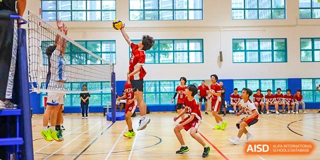 A student athlete in a red jersey performing a powerful jump spike during a volleyball game in the bright indoor gym at Guangzhou ULink International School.