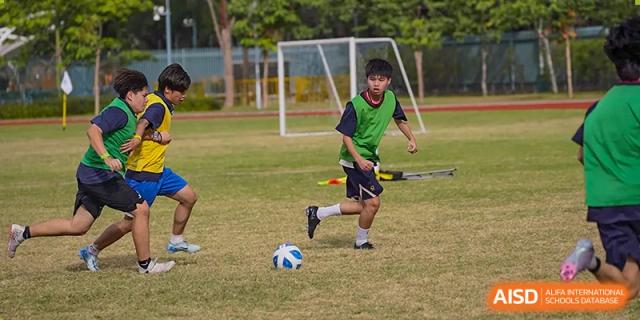 A student in a green training vest skillfully dribbling a soccer ball across the grass field during an afternoon practice at Guangzhou ULink International School.