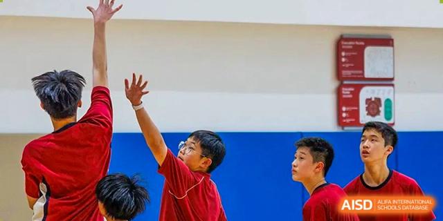 A close-up of a young student in a red sports uniform reaching upward during an indoor physical education activity at Guangzhou ULink International School.