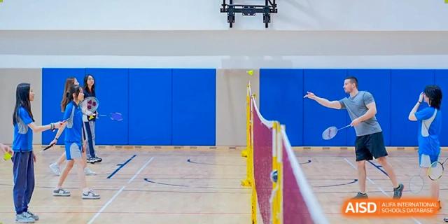 A view of an indoor badminton court with a yellow net and blue wall padding, ready for student sports and competition at Guangzhou ULink International School.