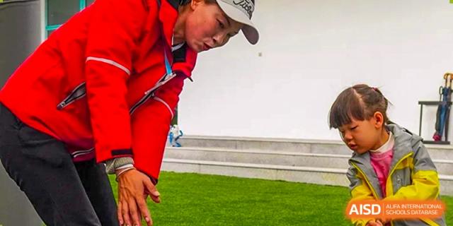 A student wearing a white cap and red jacket bends over to practice golf putting on an indoor green turf facility at Guangzhou ULink International School.