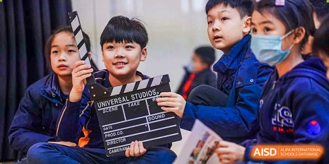 A young boy smiles while holding a movie clapboard during a creative school activity at Yew Wah International Education School of Guangzhou