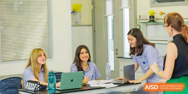 A female student with long hair smiles while working on her laptop in a modern classroom setting at Yew Wah International Education School of Guangzhou