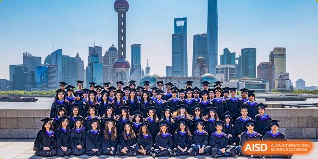 A large group of graduates in blue and black gowns pose for a photo with a city skyline in the background at Yew Wah International Education School of Guangzhou