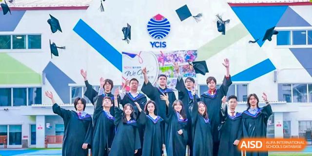 A group of graduates in blue and black gowns cheer and toss their caps into the air in front of a YCIS logo at Yew Wah International Education School of Guangzhou