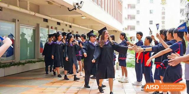 Several female graduates in black academic robes smile and walk together through an outdoor campus corridor at Yew Wah International Education School of Guangzhou