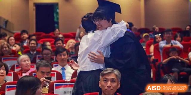 A graduate in a black gown and cap shares an emotional hug with a family member during a graduation ceremony at Yew Wah International Education School of Guangzhou