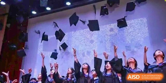 A group of students in graduation gowns toss their caps high into the air against a backdrop of a projected sky at Yew Wah International Education School of Guangzhou
