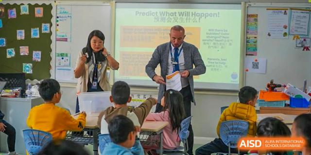 A male teacher in a grey blazer interacts with young students in a classroom during a lesson with a projector at Yew Wah International Education School of Guangzhou