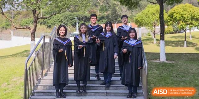 A group of four graduates in black academic gowns and caps pose for a photo on outdoor stairs on campus at Yew Wah International Education School of Guangzhou